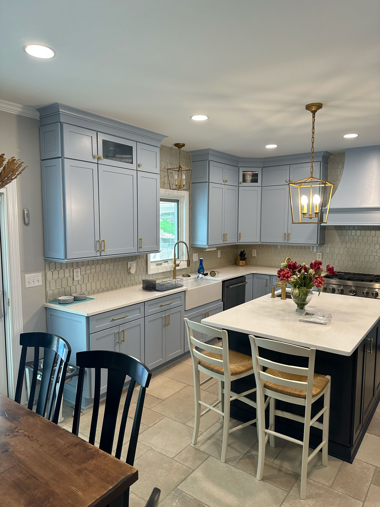 A newly renovated kitchen and dining area by Five One Eight Contracting featuring light blue-gray cabinets, white countertops, and gray patterned backsplash.