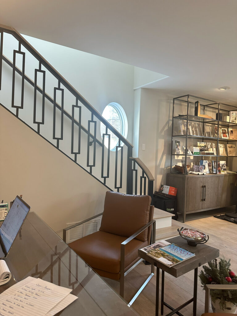 Modern office interior with a sleek metal staircase, brown leather chair, and glass topped desk.